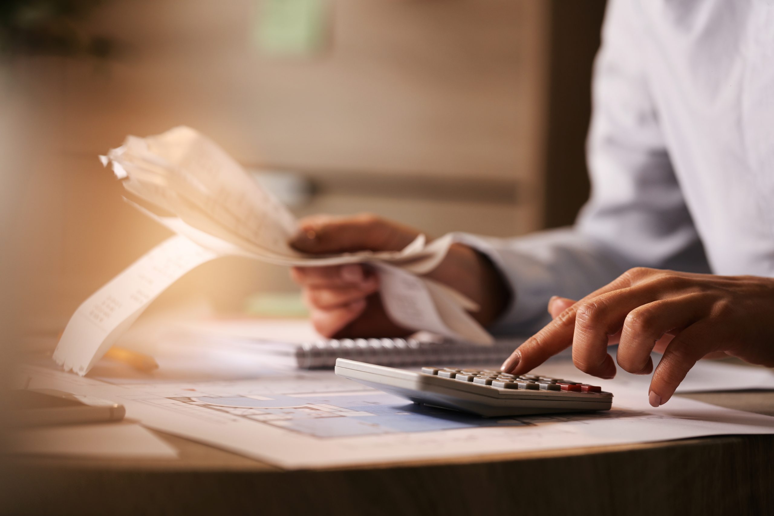 Close-up of economist using calculator while going through bills and taxes in the office.